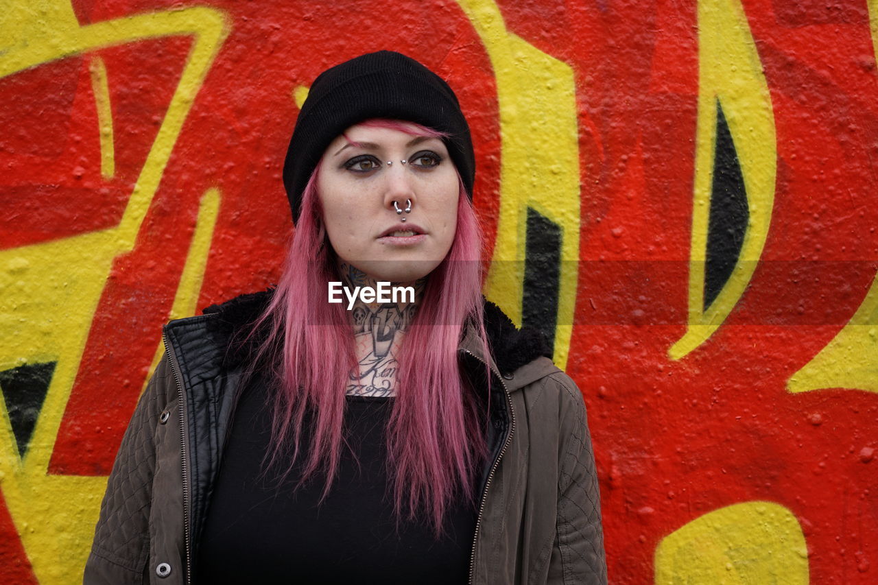 Young woman with pink hair standing against graffiti wall