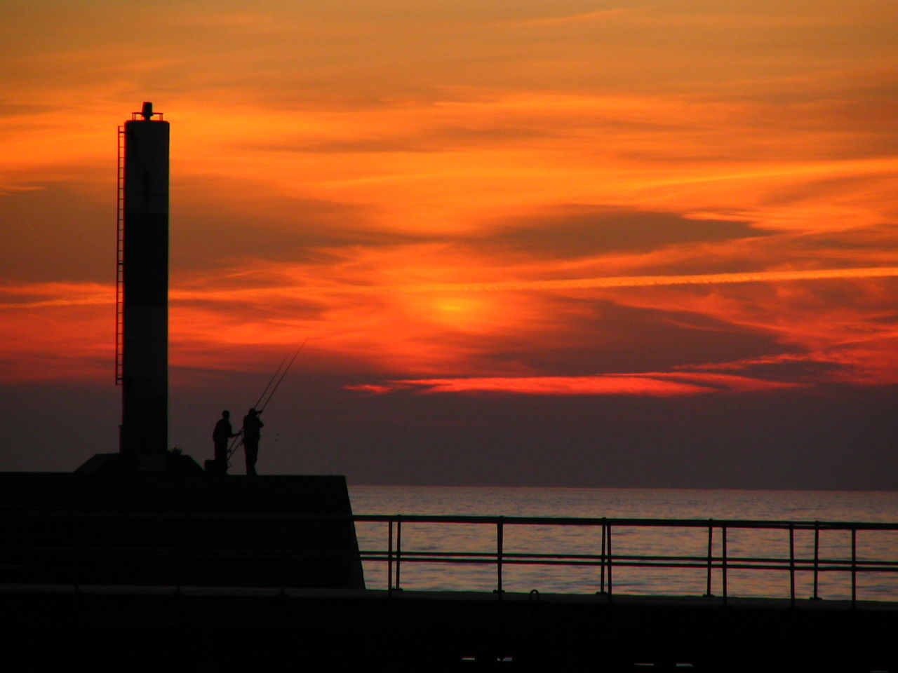 Silhouette fishermen fishing against orange sky