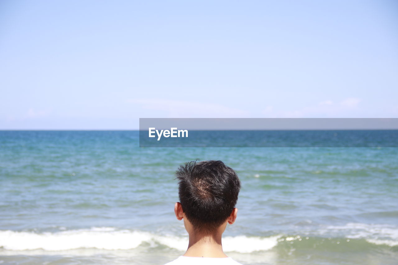 Rear view of man looking at beach against sky