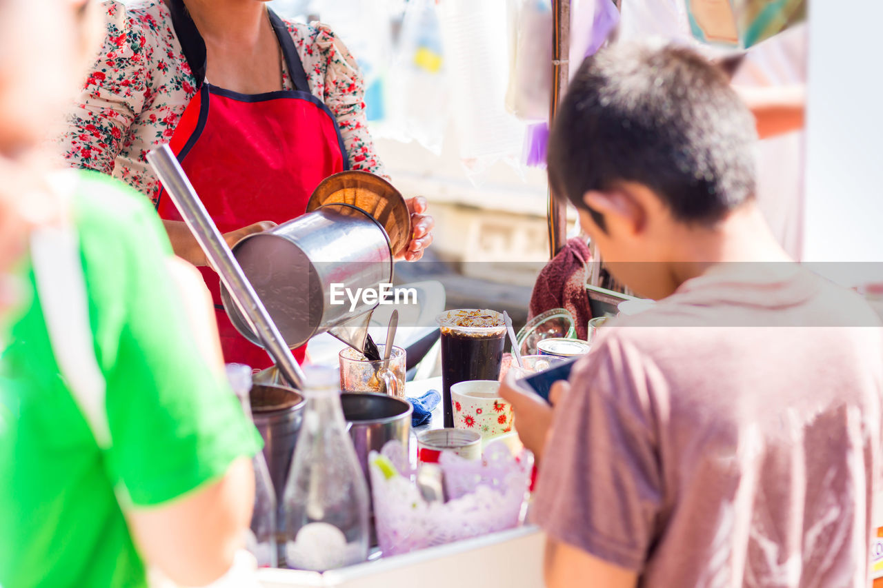 Rear view of mother and son standing by ice cream stall in city