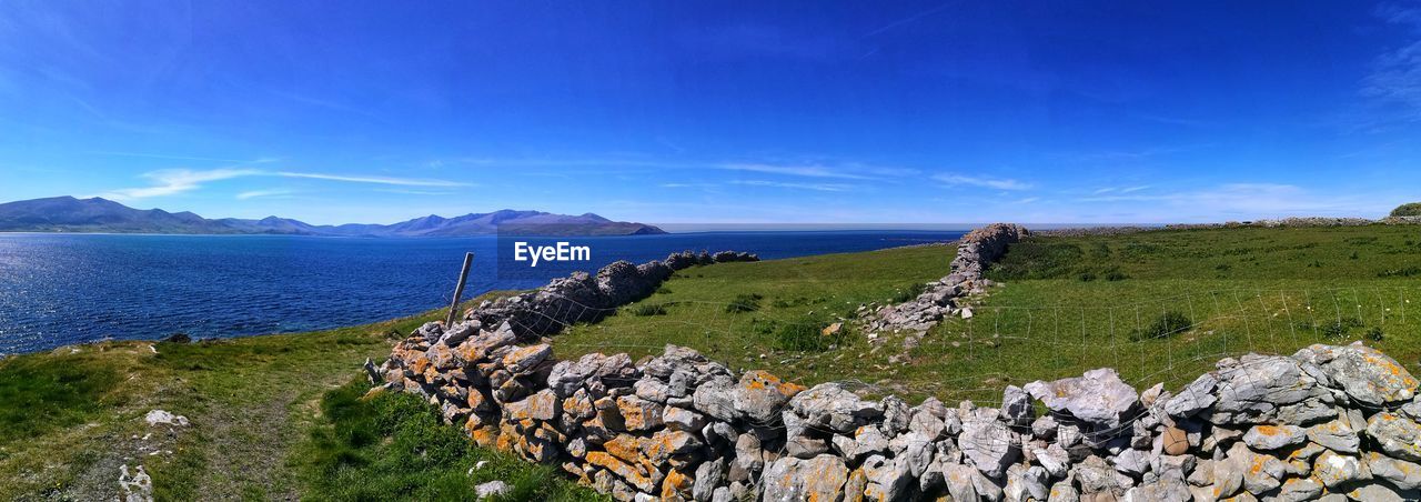 Scenic view of sea against blue sky with stone wall. county kerry. ireland.