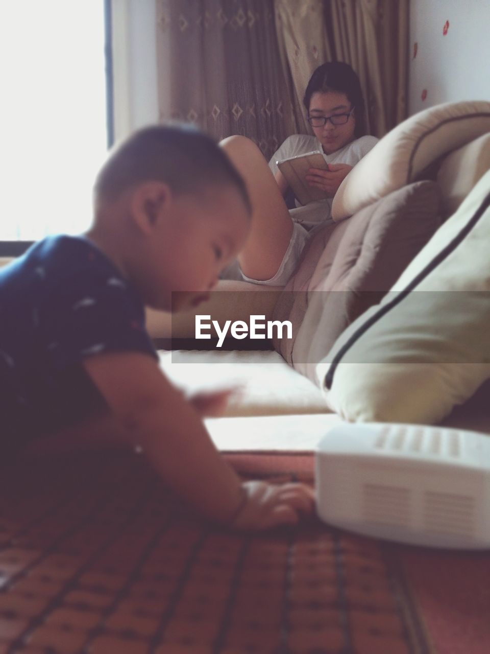 Boy by sofa with sister using digital tablet in living room at home