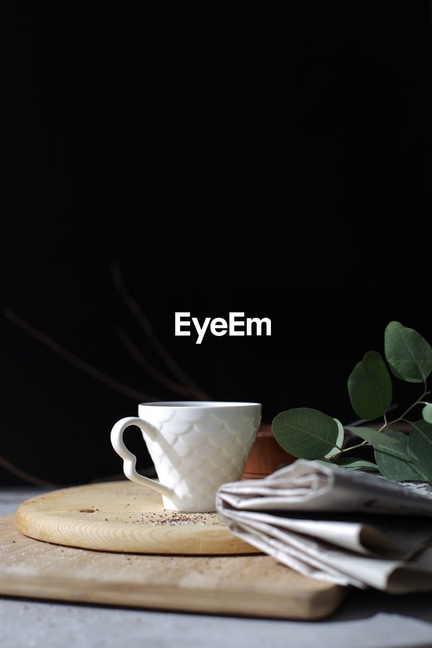 Coffee cup with newspaper on table against black background