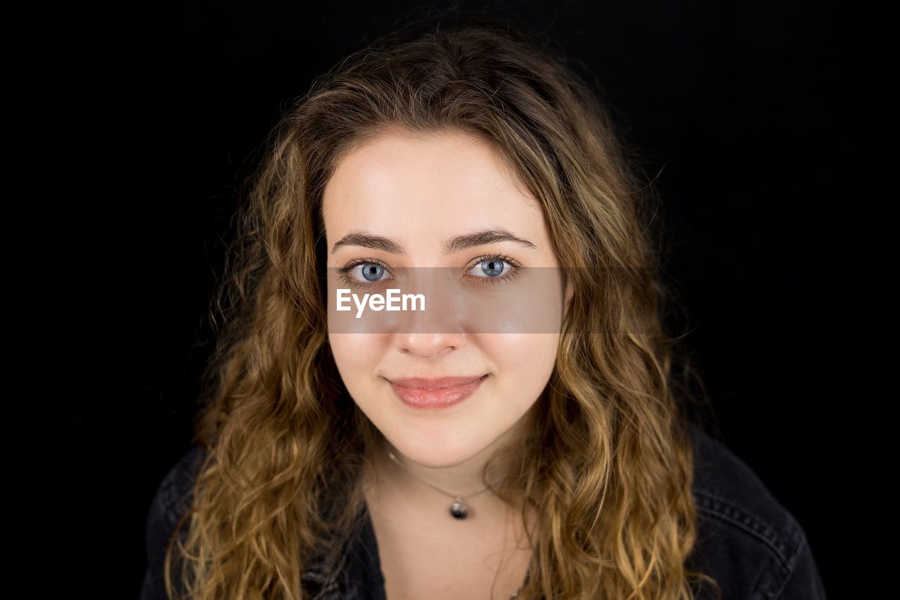 PORTRAIT OF YOUNG WOMAN AGAINST BLACK BACKGROUND