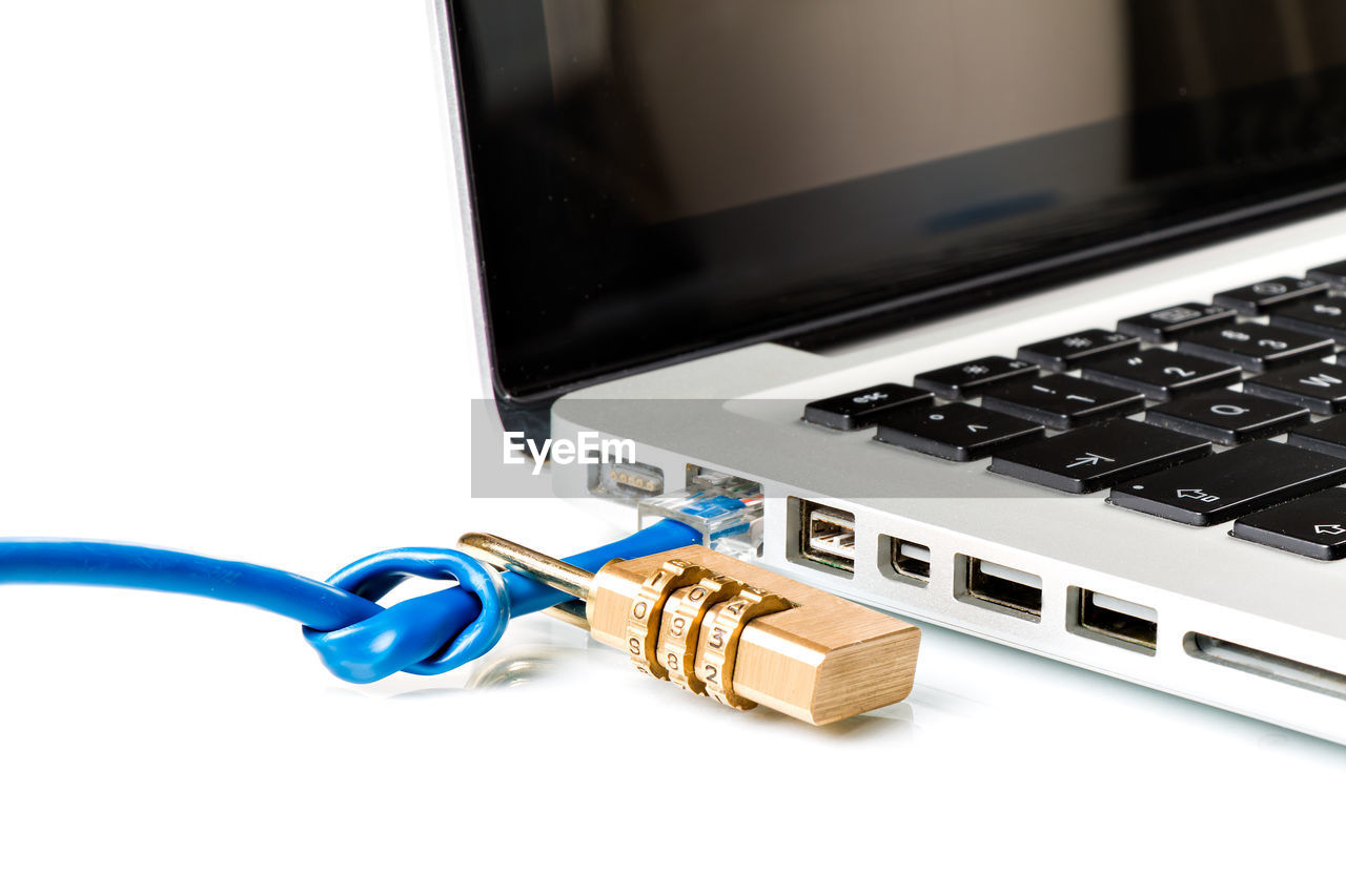 Close-up of padlock and cable on computer keyboard against white background