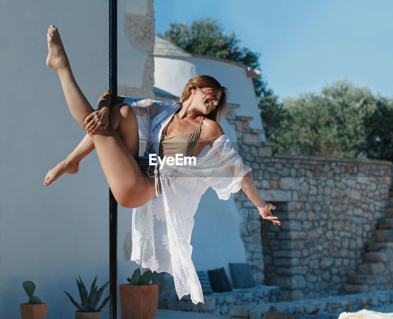 Young pole dancer posing on a portable platform against the villa wall. 