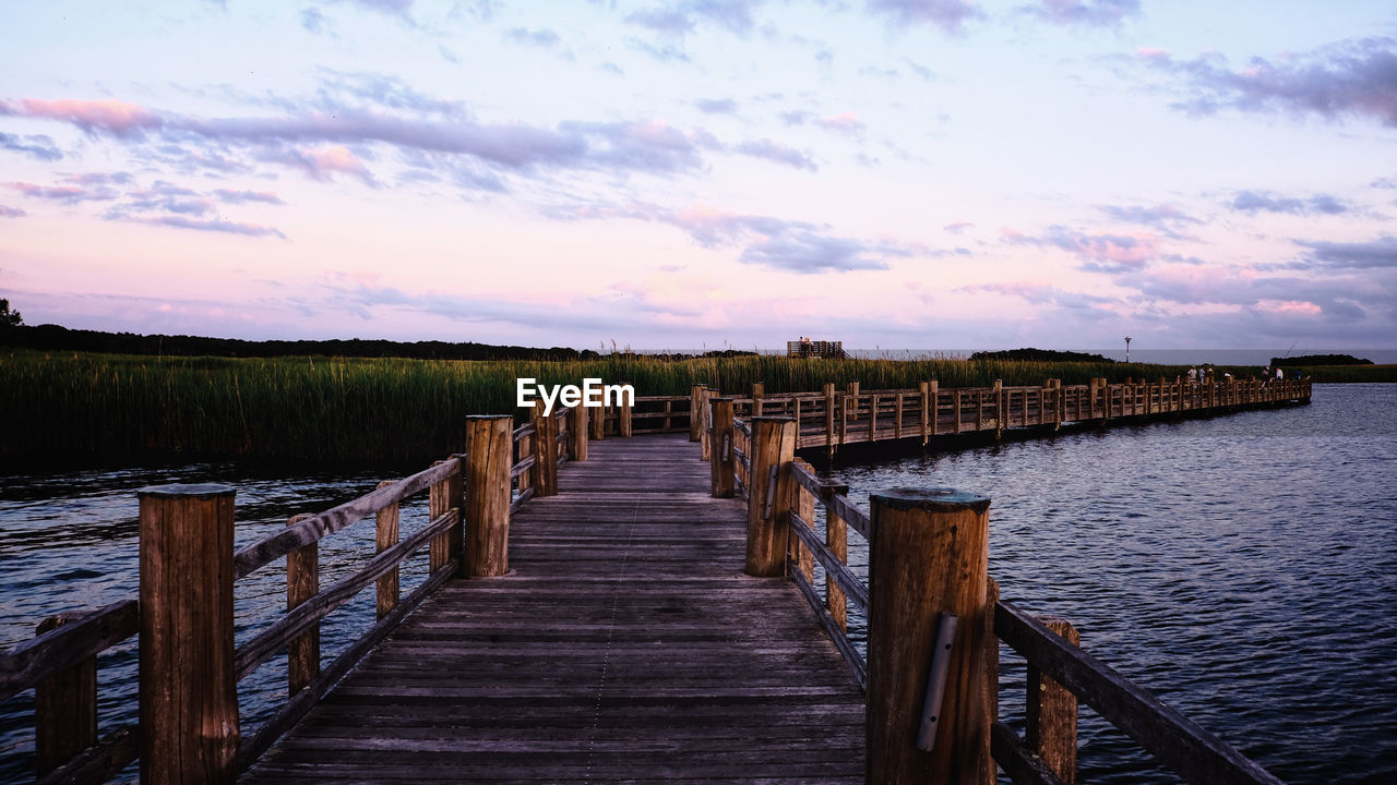 Wooden pier on jetty leading towards sea against sky