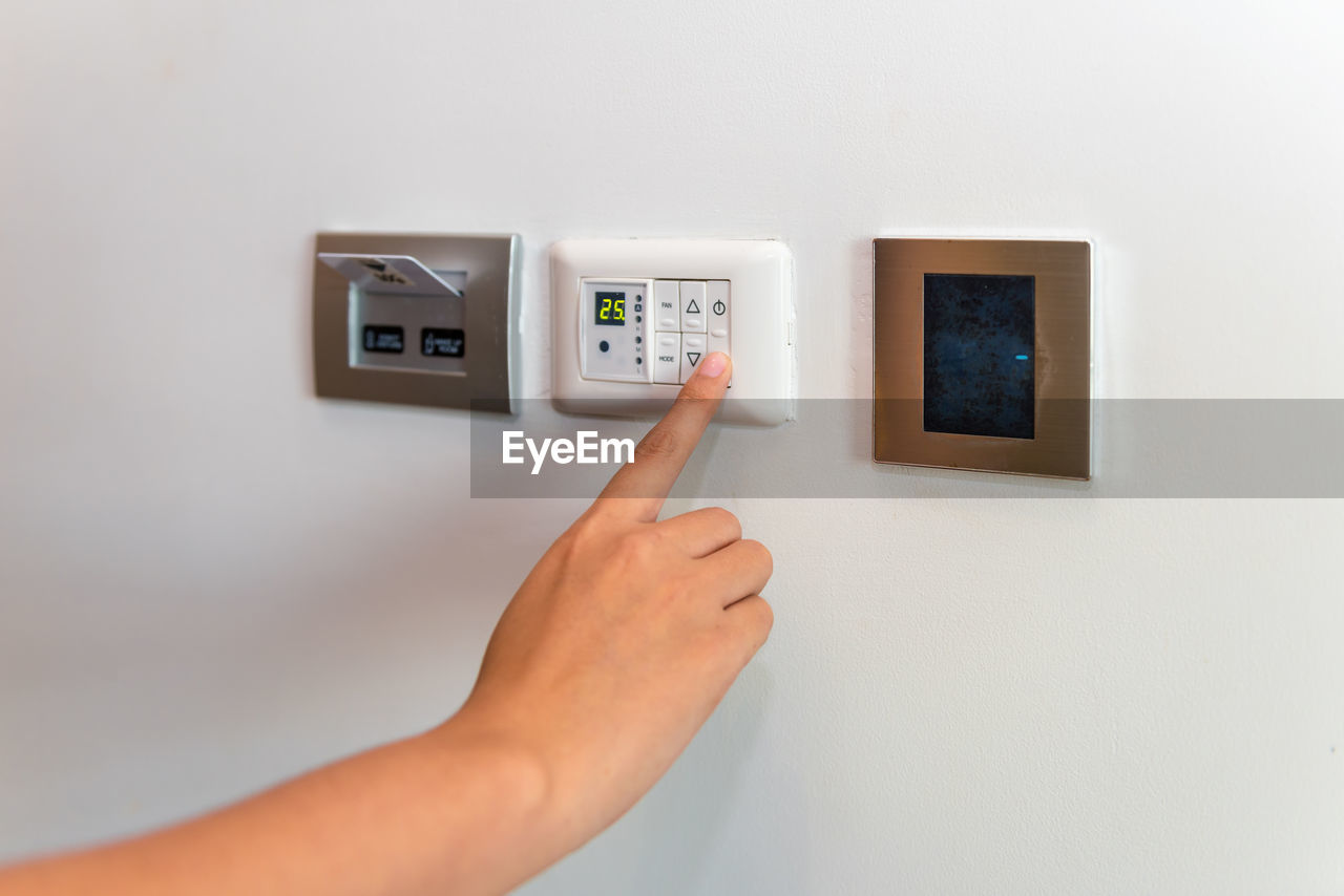 Close-up of human hand using air conditioner remote on white wall at home