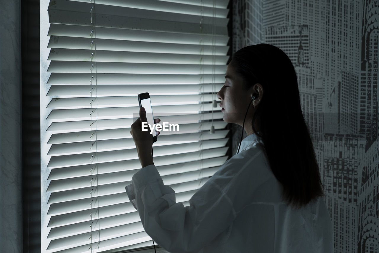 PORTRAIT OF YOUNG WOMAN LOOKING THROUGH WINDOW