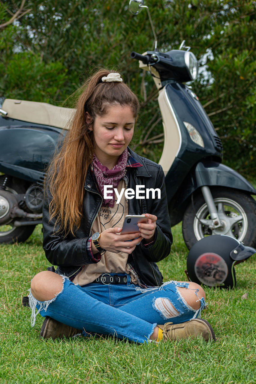 Young woman using a smartphone while standing by her motorbike
