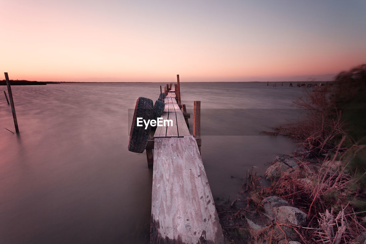 Tires hanging on old wooden jetty over salton sea lake against sky