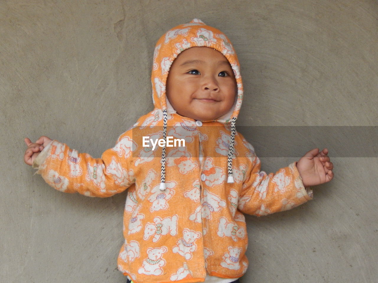 Portrait of smiling baby boy in warm clothing standing against concrete wall