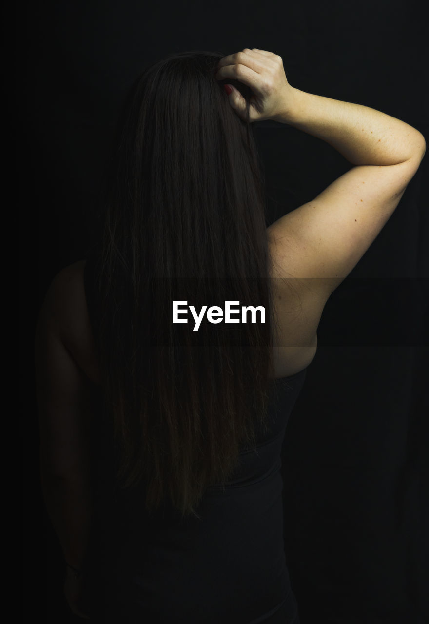 Brunette girl is on her back touching her hair. black background. studio photograph. 