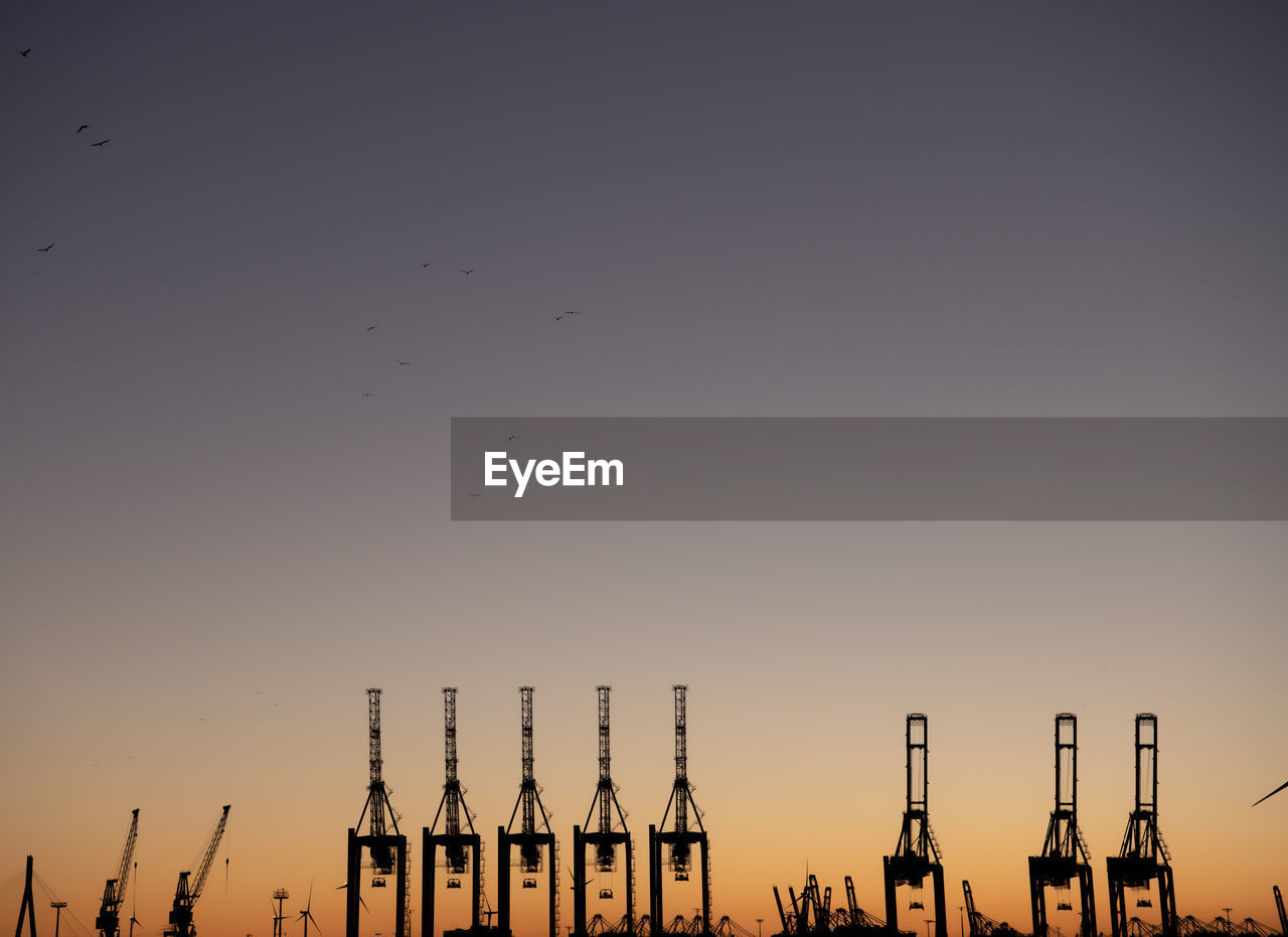 SILHOUETTE CRANES AGAINST CLEAR SKY AT SUNSET