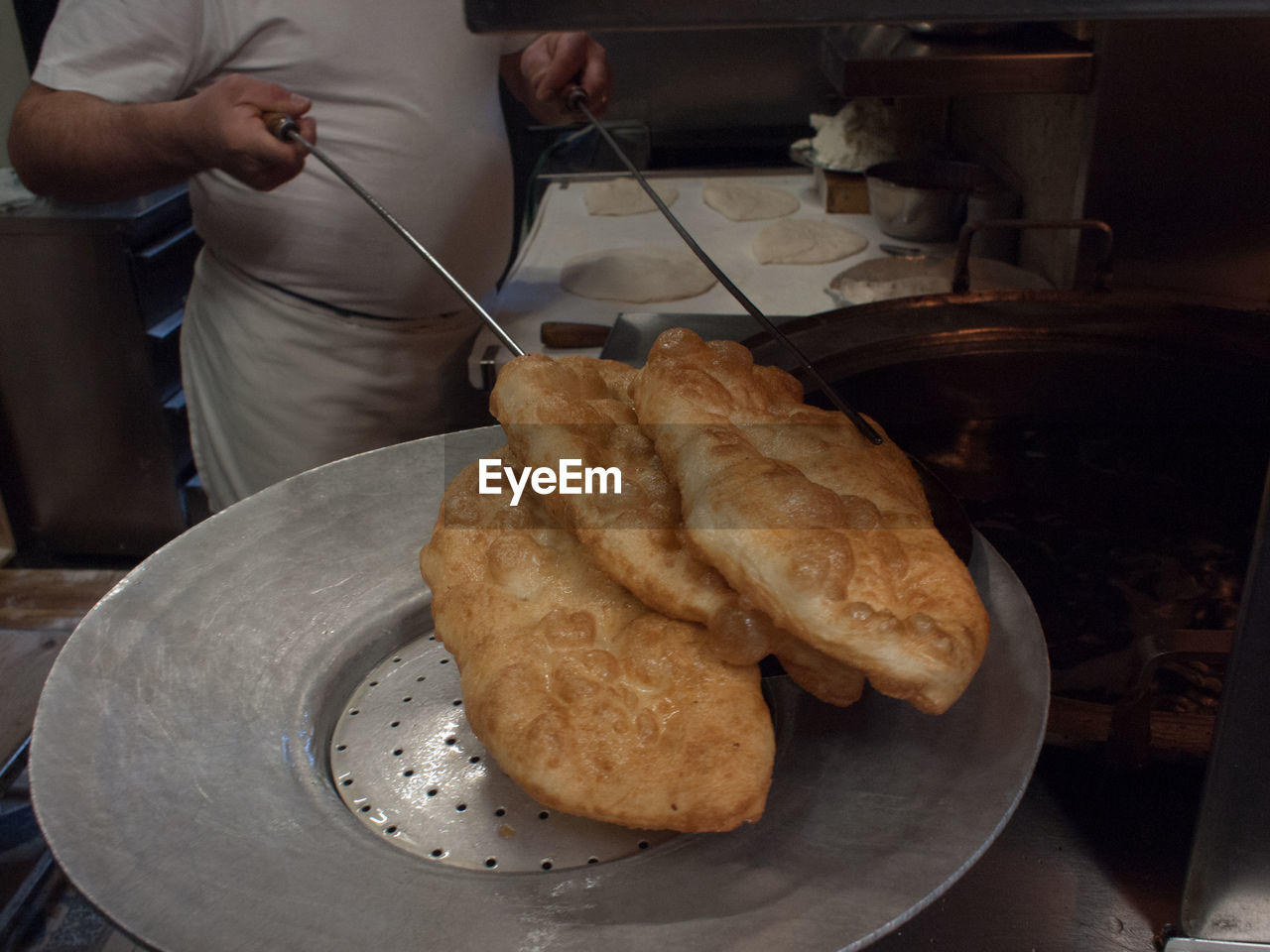 Midsection of chef holding fresh fried breads on plate in commercial kitchen