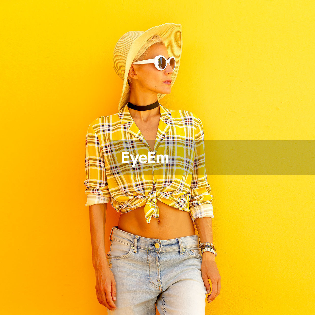 Woman wearing hat looking away while standing against yellow wall