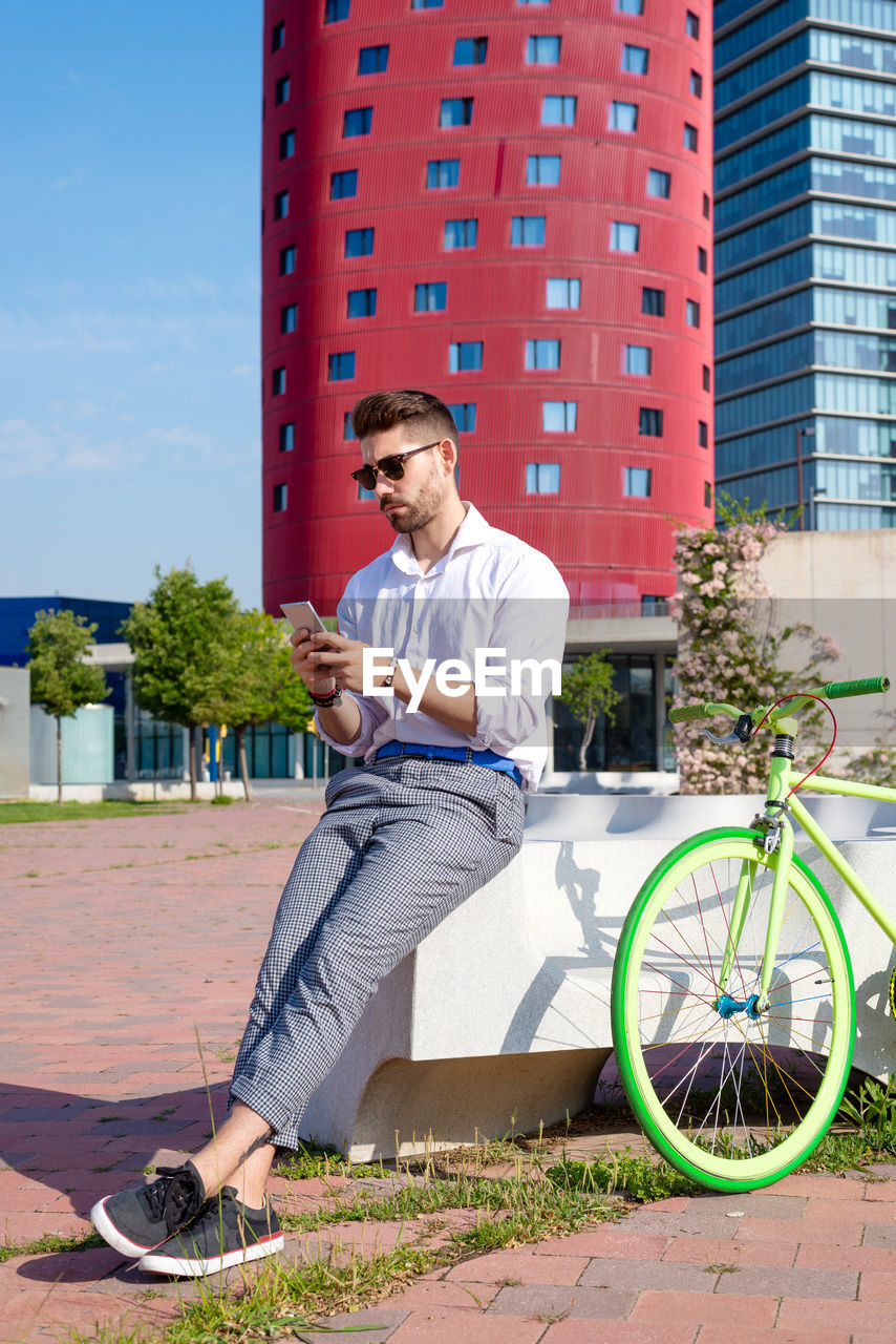 Outdoor portrait of handsome young man with mobile phone and fixed gear bicycle in the street.