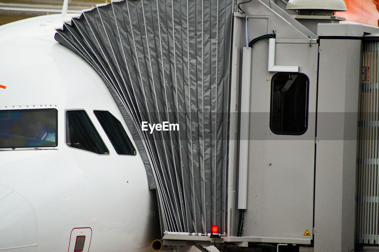 Cropped image of airplane with passenger boarding bridge at airport