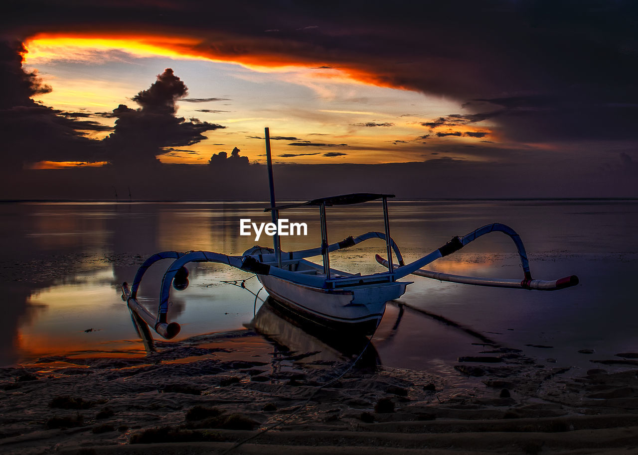 BOAT MOORED ON SHORE AGAINST SKY DURING SUNSET