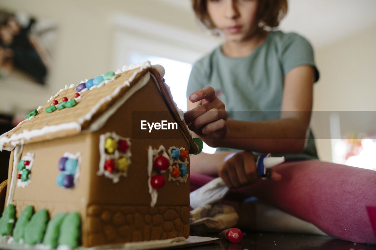 Low angle view of girl making gingerbread house on table at home
