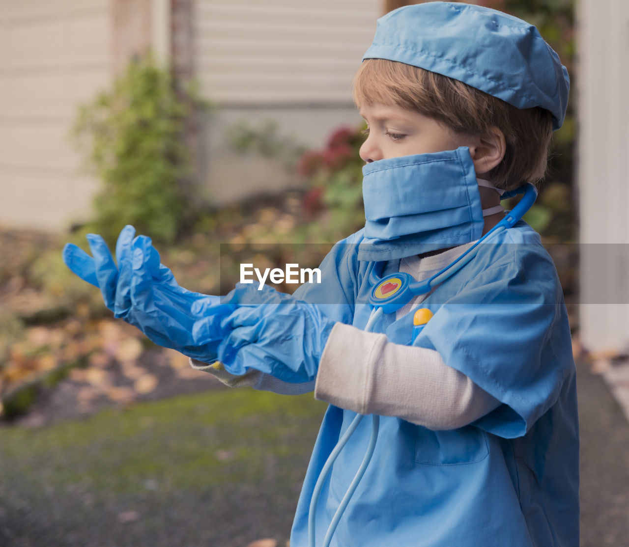 Boy in doctor costume wearing gloves while standing in yard