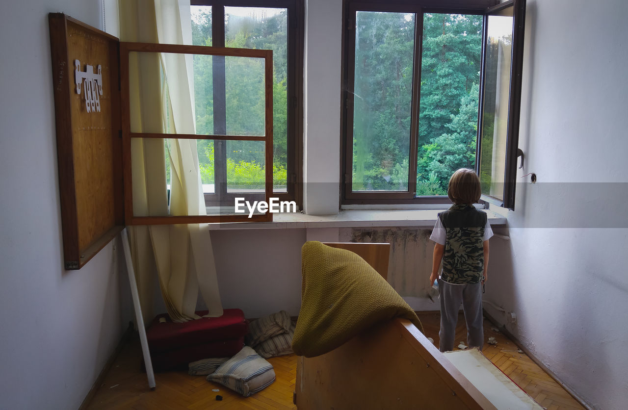 Rear view of boy looking through window at home