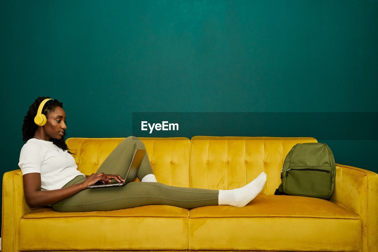 Afroamerican student laying at a yellow sofa front a dark green wall