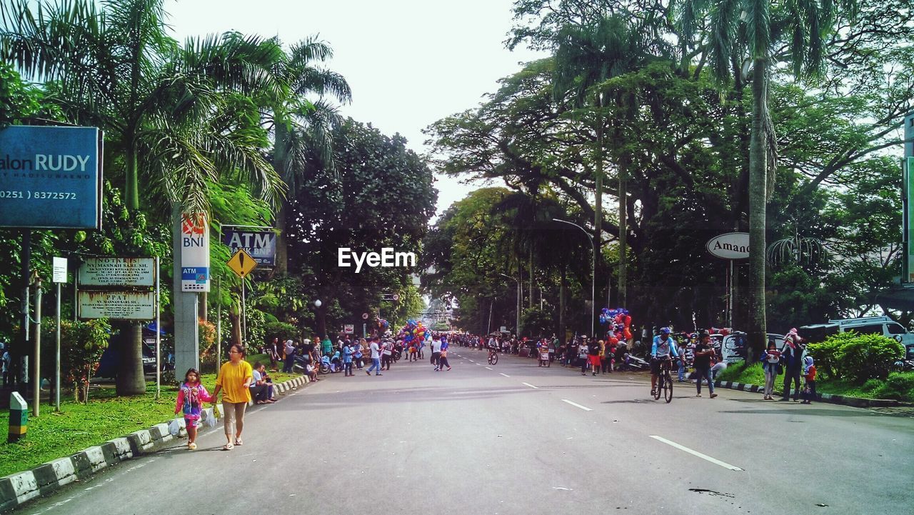 PEOPLE WALKING ON ROAD AGAINST TREES