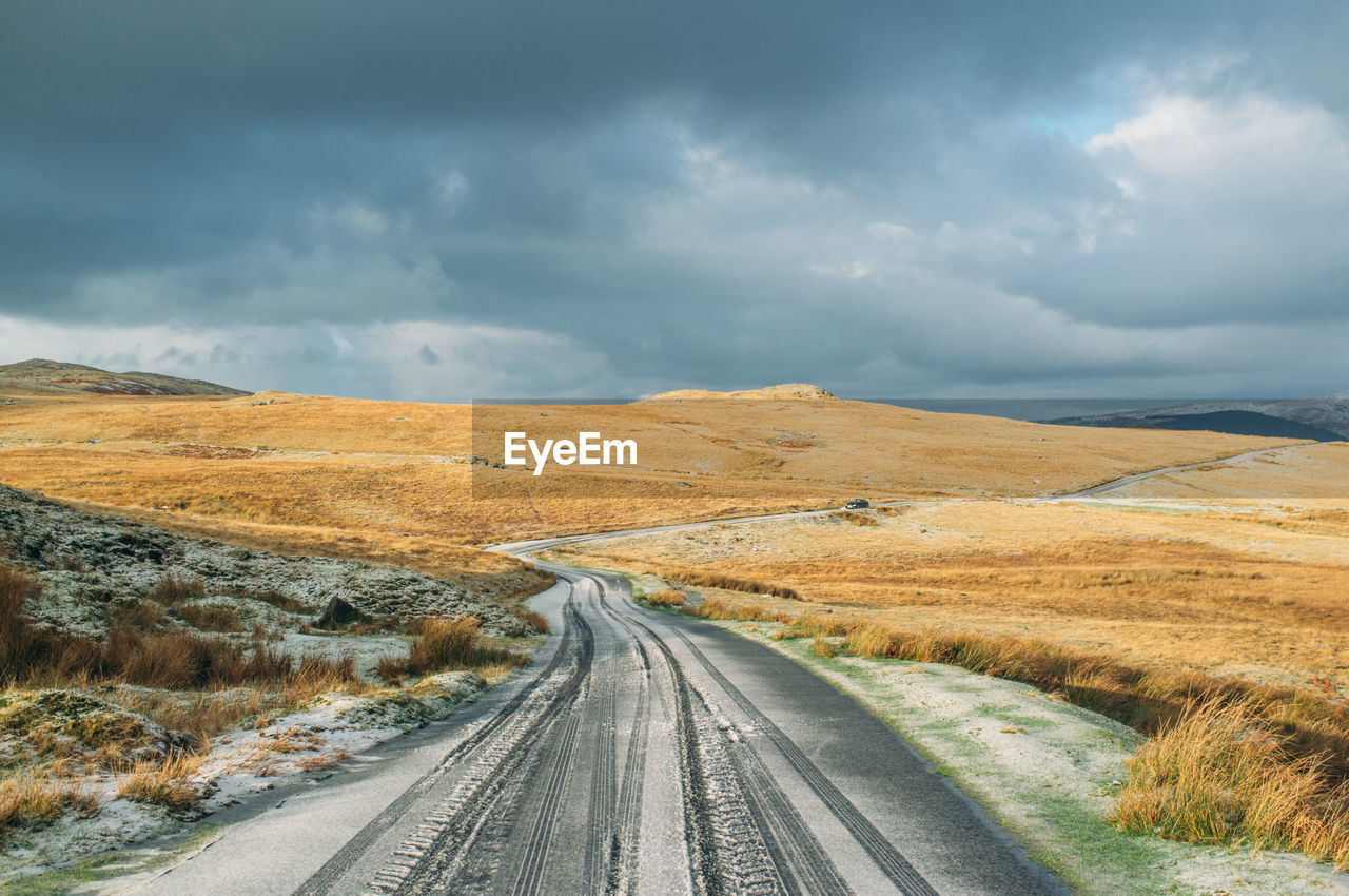 Country road on field against cloudy sky