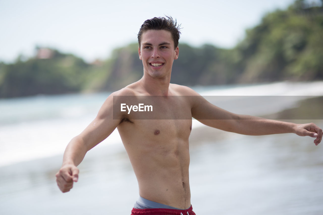 Happy young man with arms outstretched looking away at beach