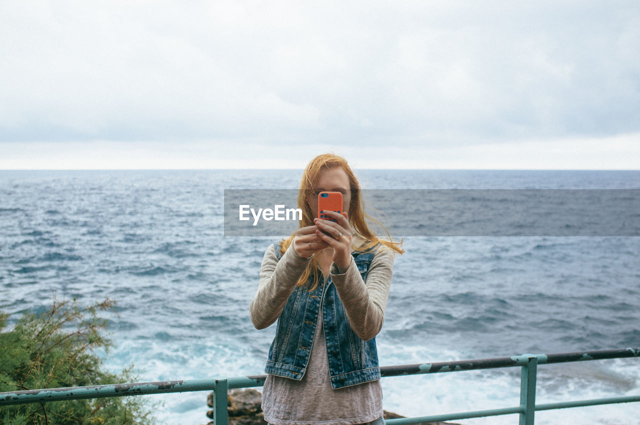 Young woman on promenade photographing with smart phone