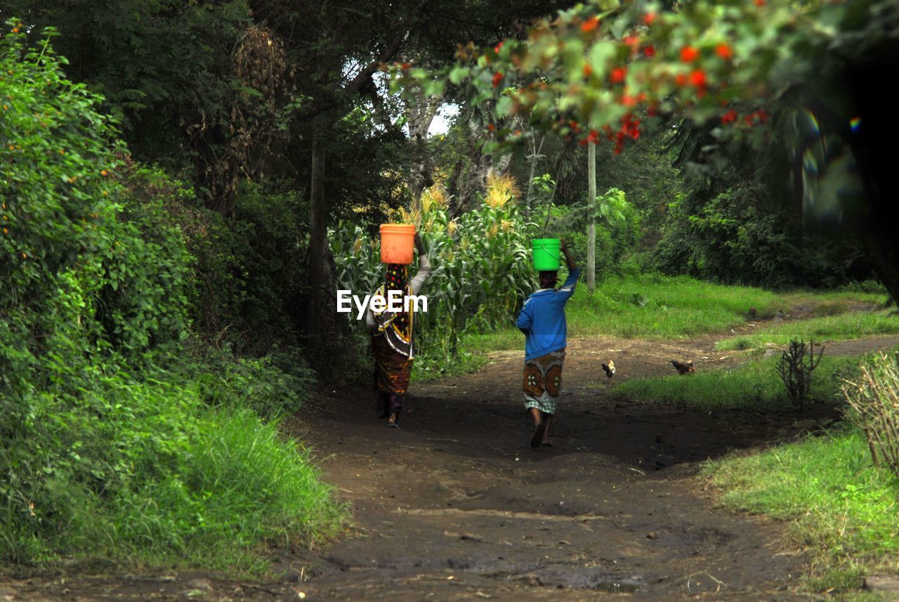 Full length rear view of women with bucket on head walking on dirt road