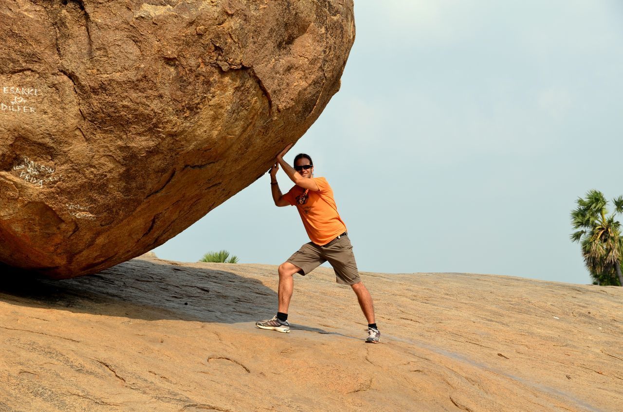 Optical illusion of young man pushing large stone against sky
