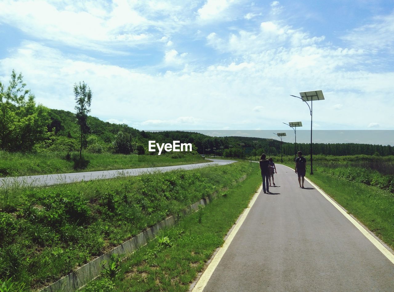 REAR VIEW OF PEOPLE WALKING ON ROAD AGAINST SKY