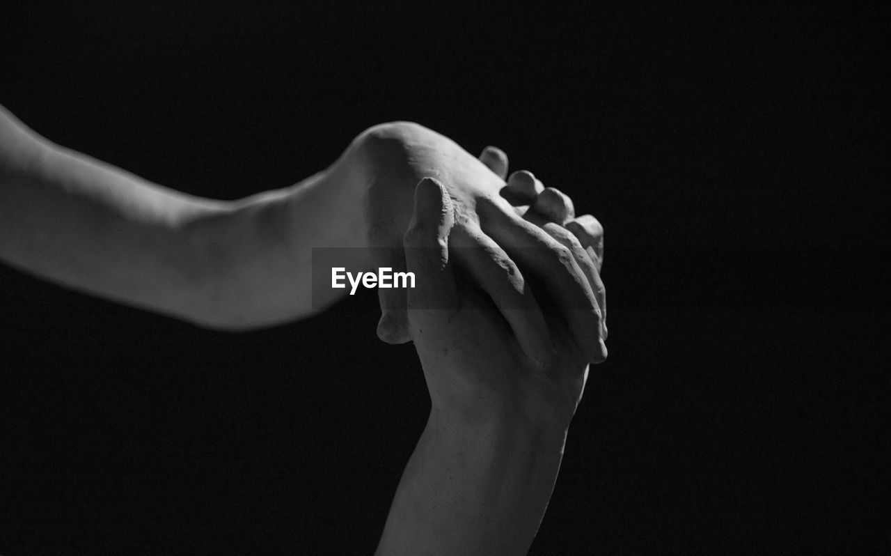 Close-up of hand holding leaf over black background