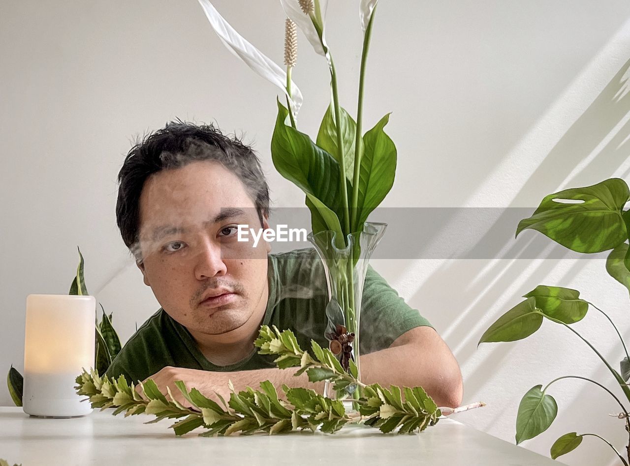 Portrait of young asian man with aromatherapy diffuser, peace lilies in vase and plants.