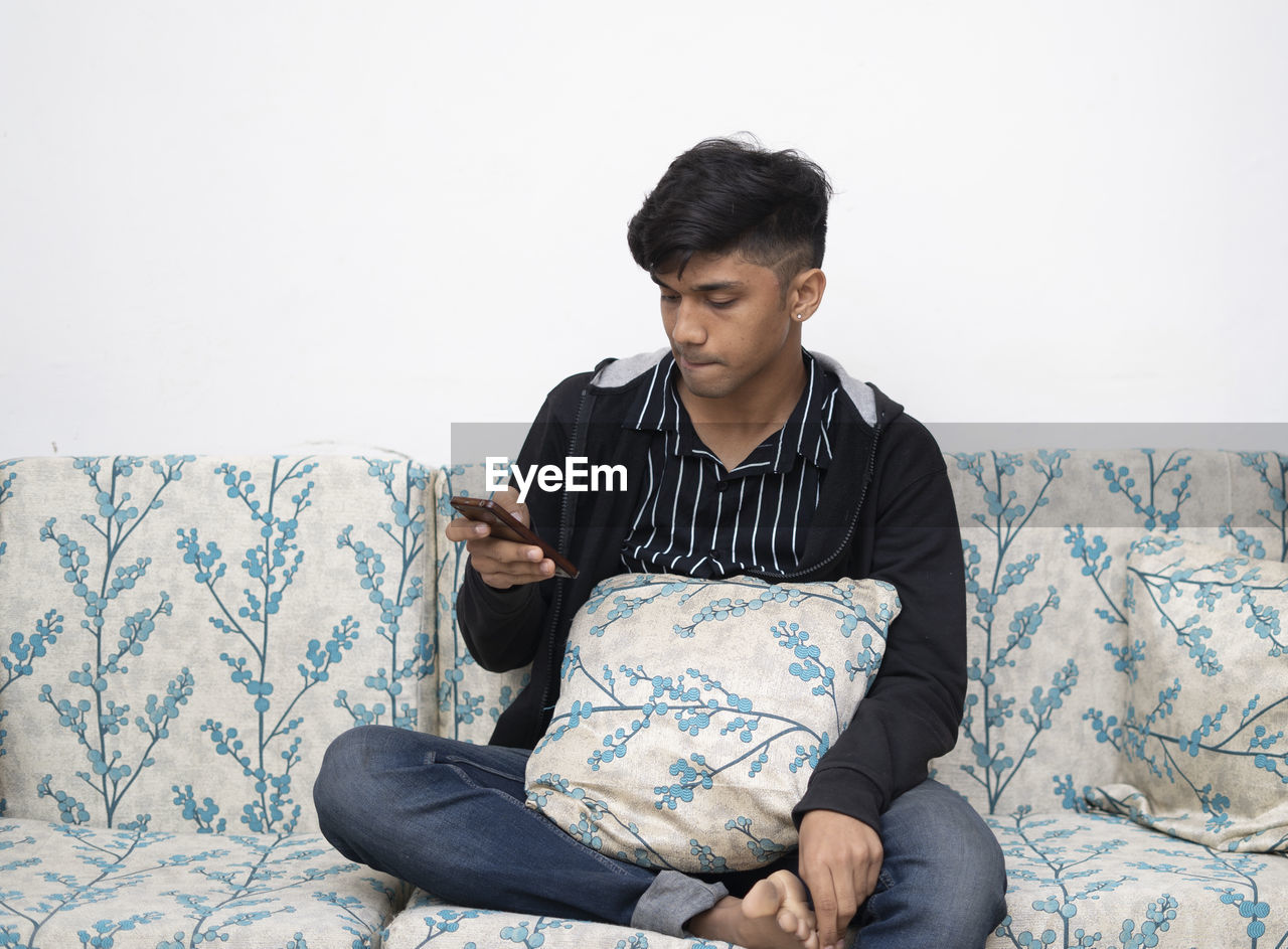 Man is using a smartphone for the internet while relaxed sitting on the sofa at his modern home.