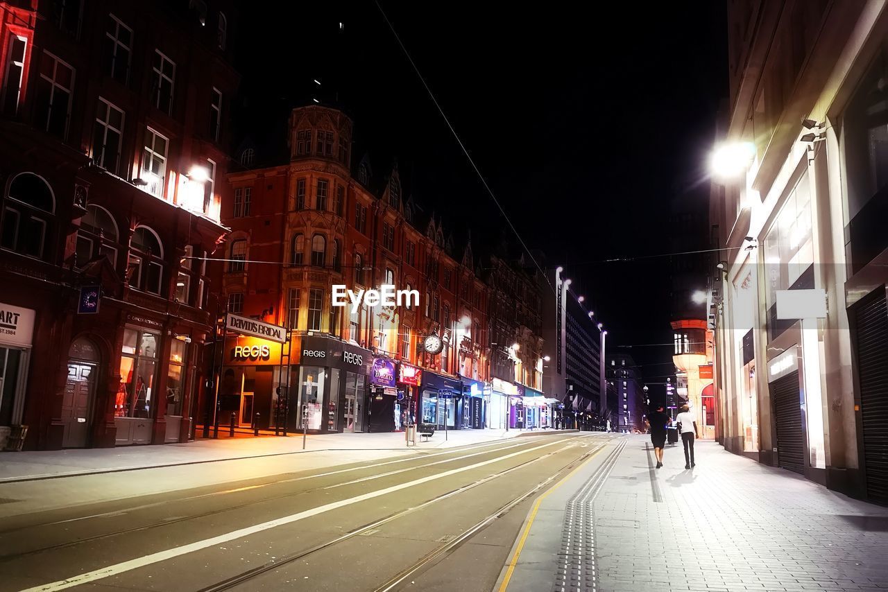 CITY STREET AMIDST ILLUMINATED BUILDINGS AT NIGHT