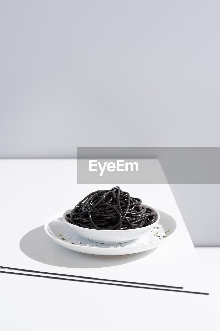 From above of ceramic bowl with delicious spaghetti with black squid ink with chopsticks on grey background