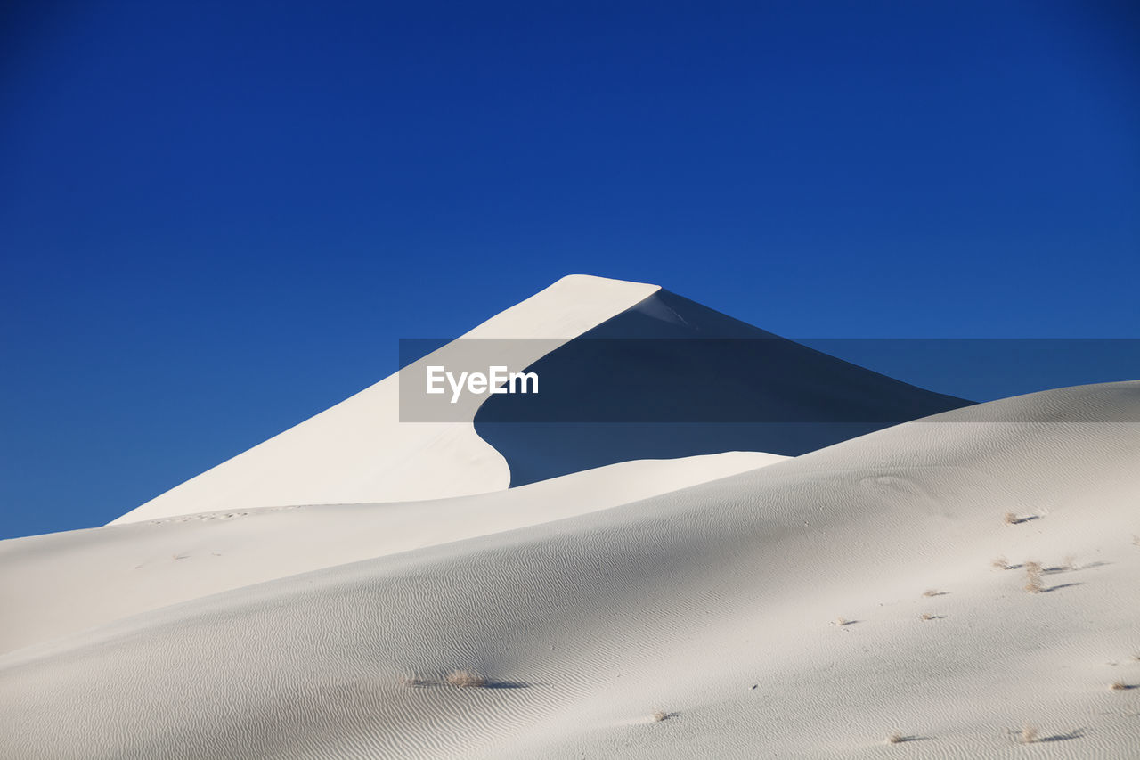 Low angle view of desert against clear blue sky