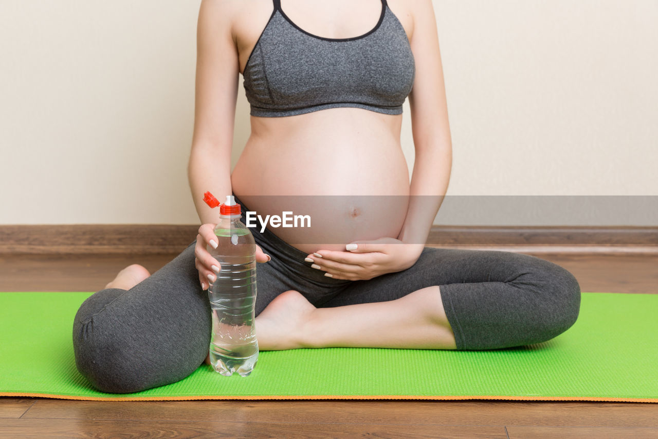 MIDSECTION OF WOMAN SITTING BY BOTTLE WITH BABY