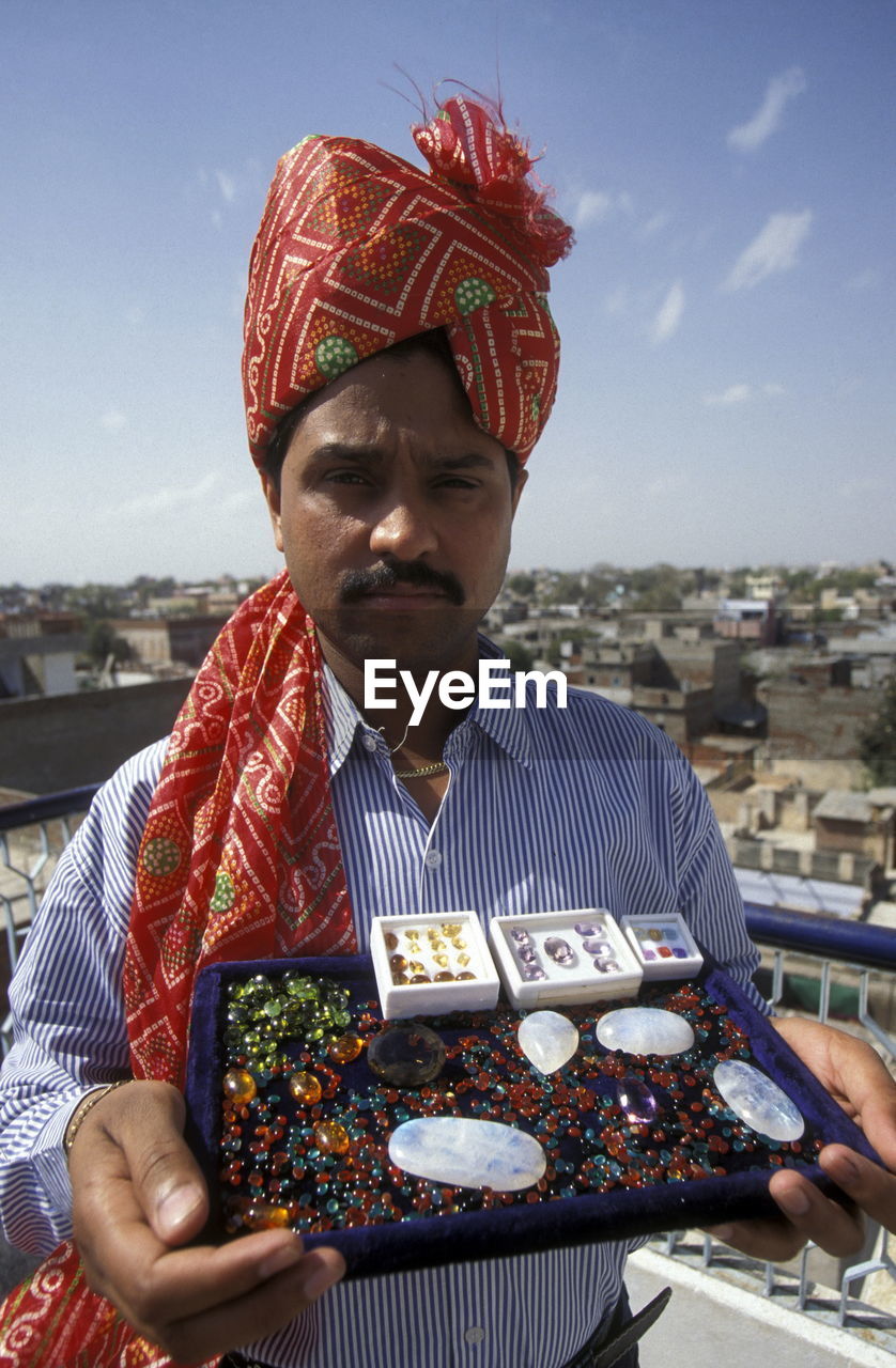 Portrait of vendor holding semi-precious gems against sky