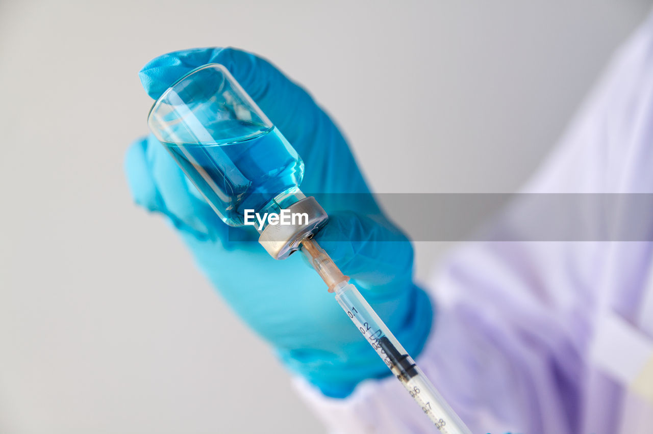 Close-up of doctor holding syringe against white background