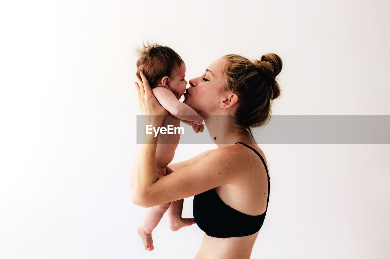 Woman kissing while holding daughter against white background