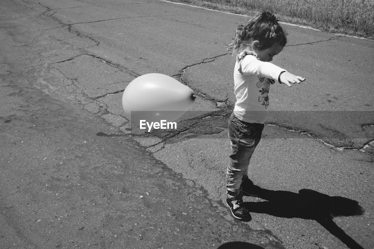 Full length side view of girl standing by helium balloon in mid-air on road