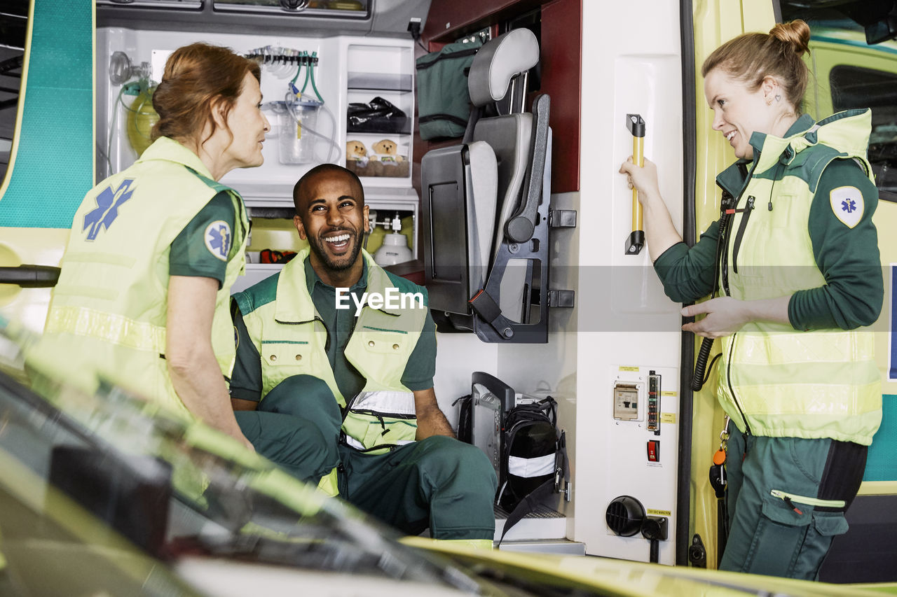 Happy multi-ethnic paramedics talking while sitting in ambulance at parking lot