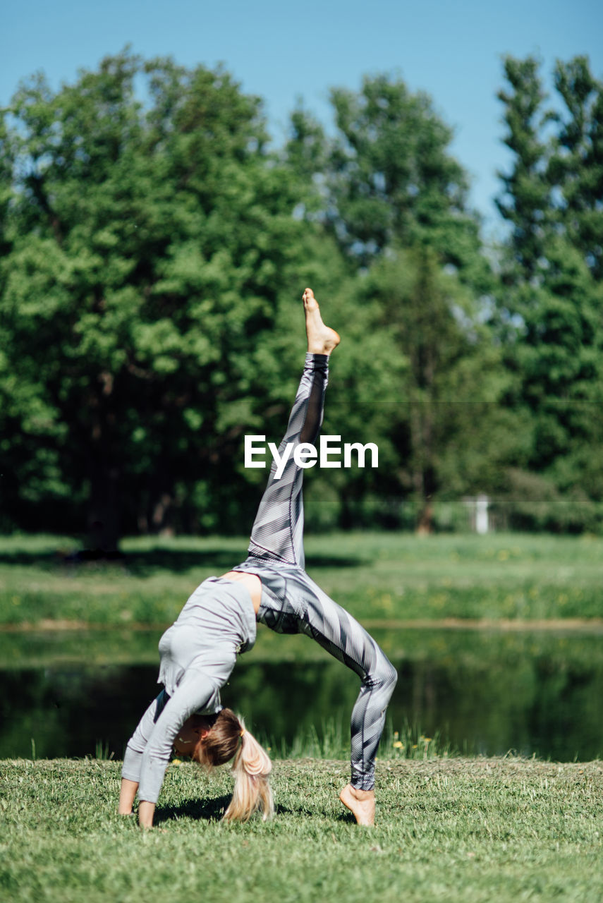 Full length of young woman exercising by pond on field