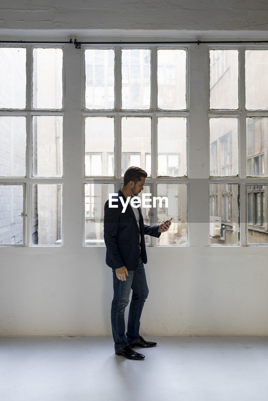 Businessman standing in a loft at the window using cell phone