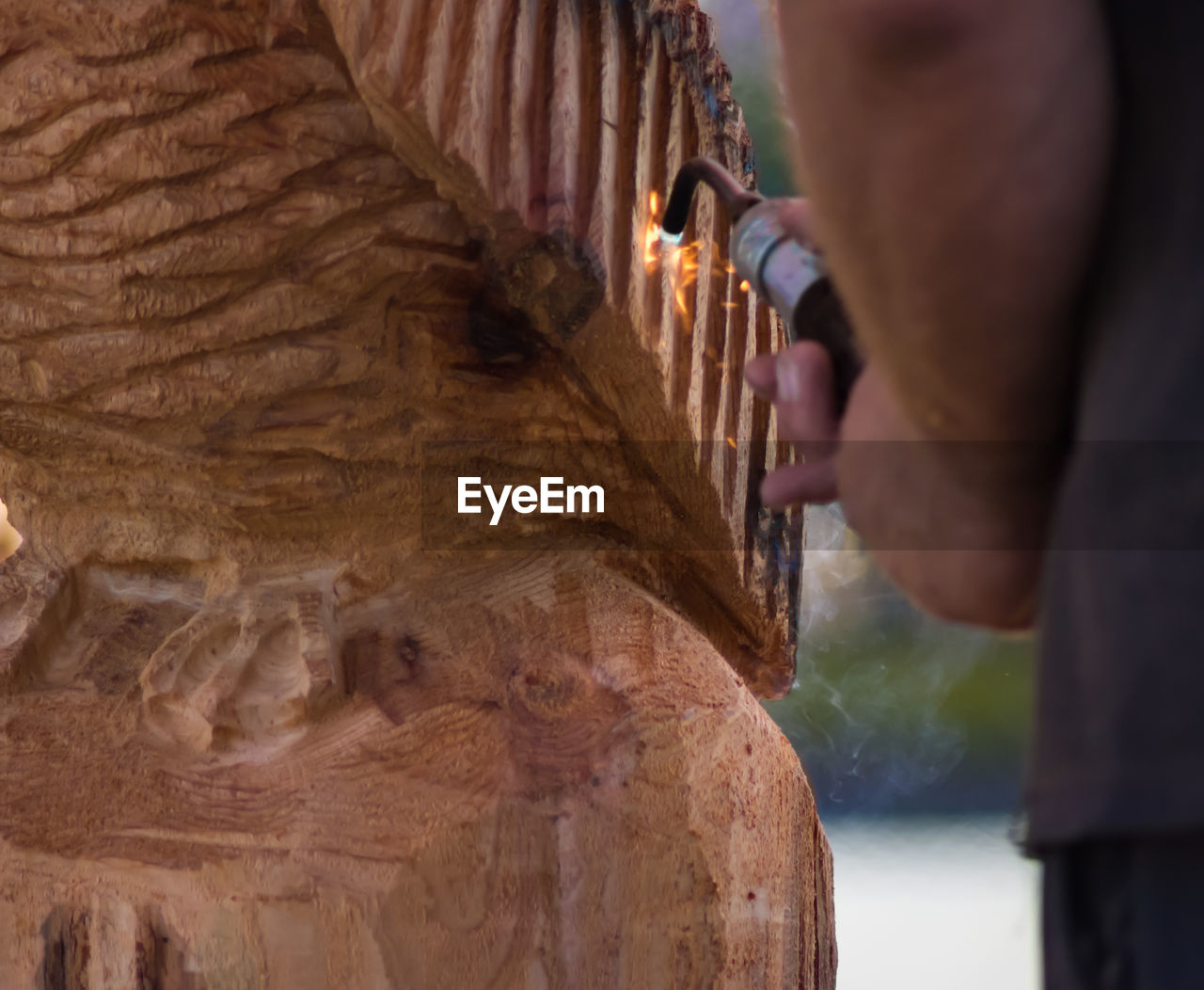 Cropped image of man using blow torch on wooden sculpture