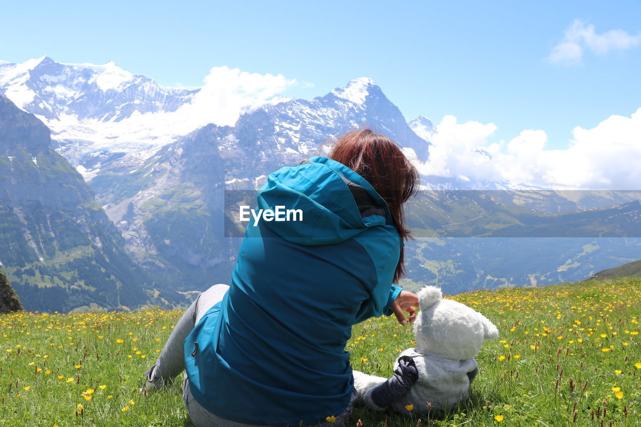 Rear view of woman sitting with stuffed toy against mountain range